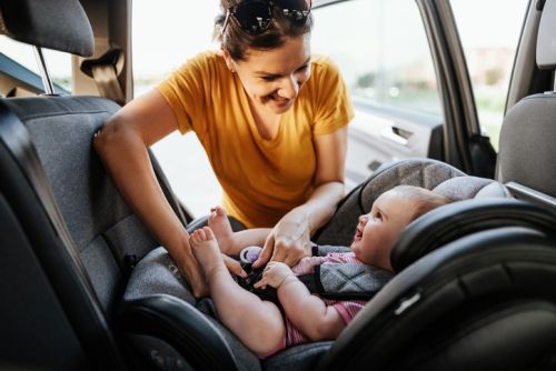 Mother putting baby girl in baby car seat concept